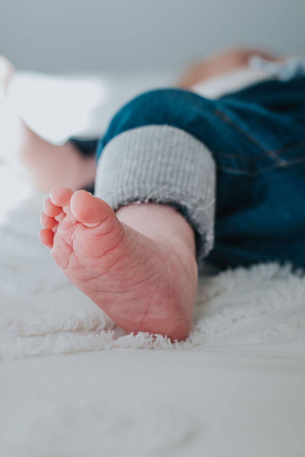 Peachy newborn foot faces the camera as baby lays on the bed.