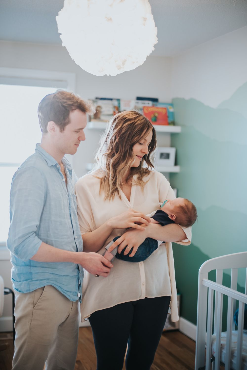 A mother and father stands holding their newborn in the nursery.
