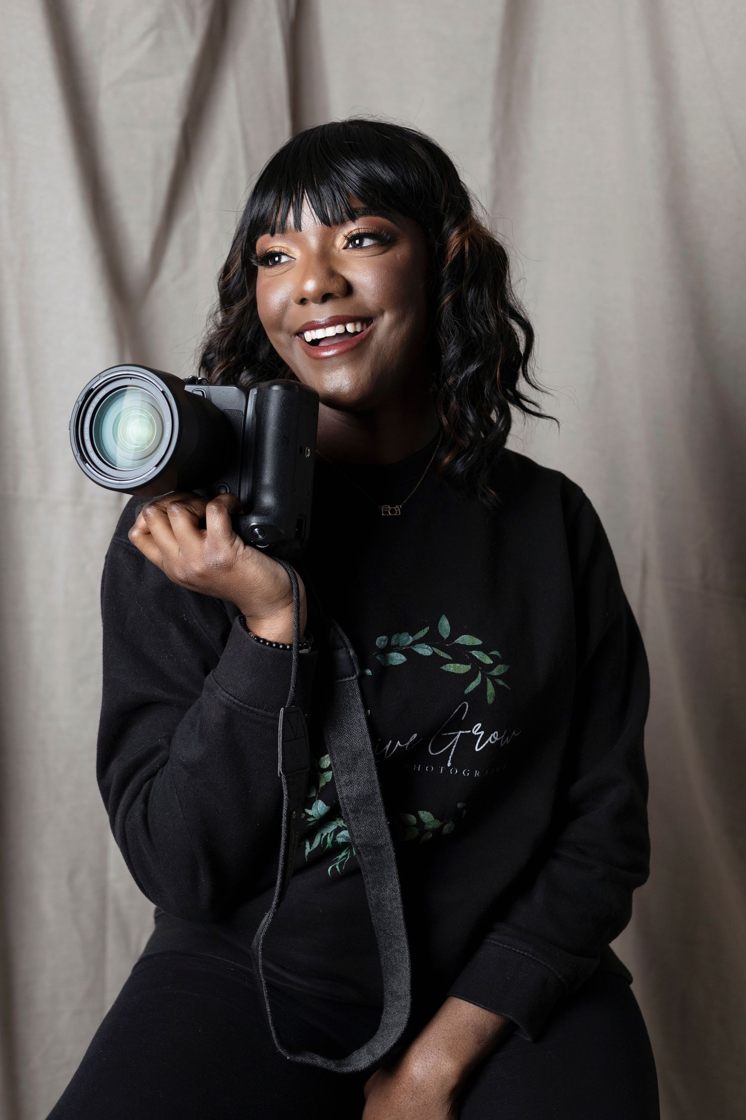 Portrait of photographer holding professional camera while wearing black sweatshirt.