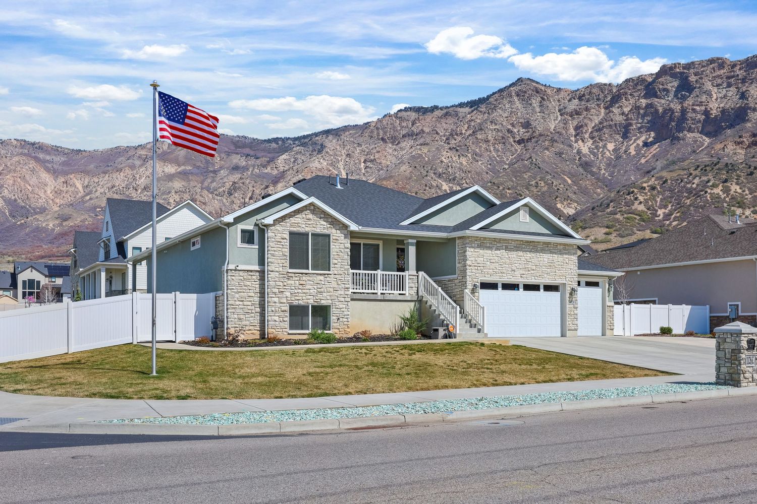 Single-story brick and gray siding home with a three-car garage, American flag, and mountain backdrop. Captured by Slate Media (best in UT)