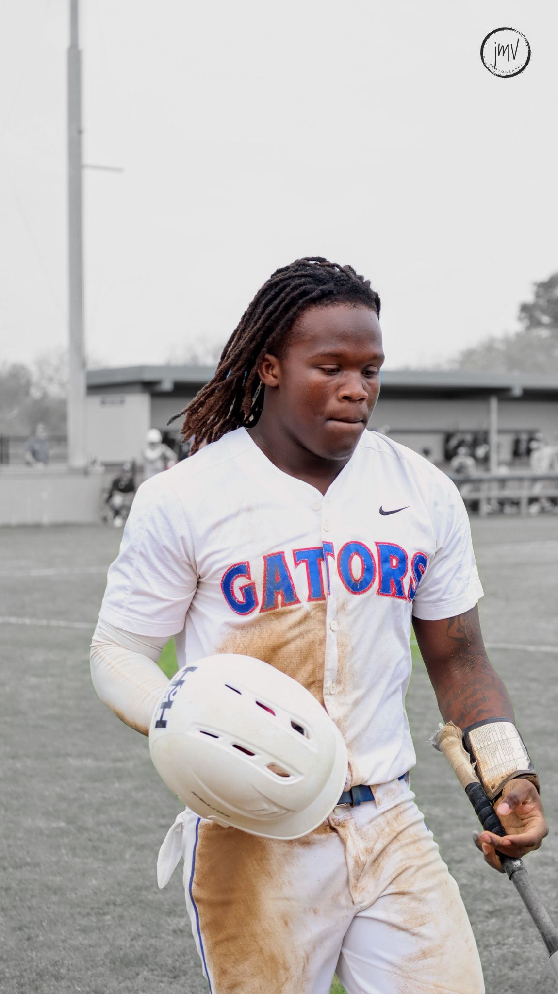 Football player in white Gators uniform carrying equipment across a field in black and white photography.