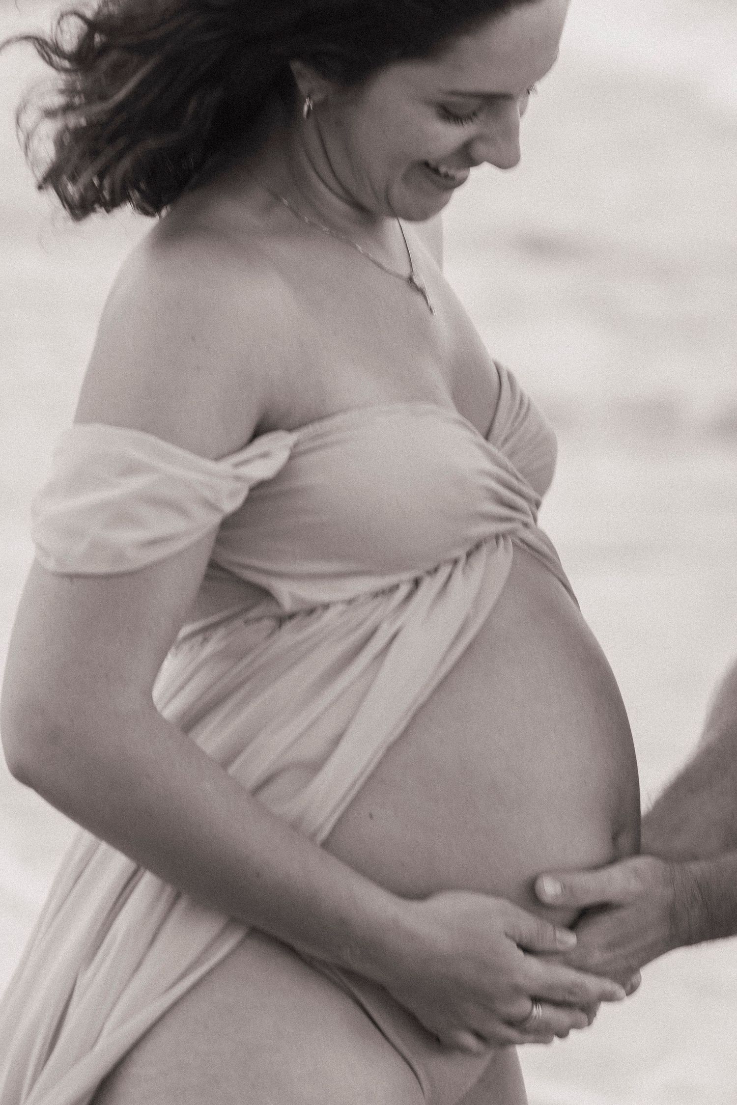 Black and white maternity portrait showing woman cradling her pregnant belly.