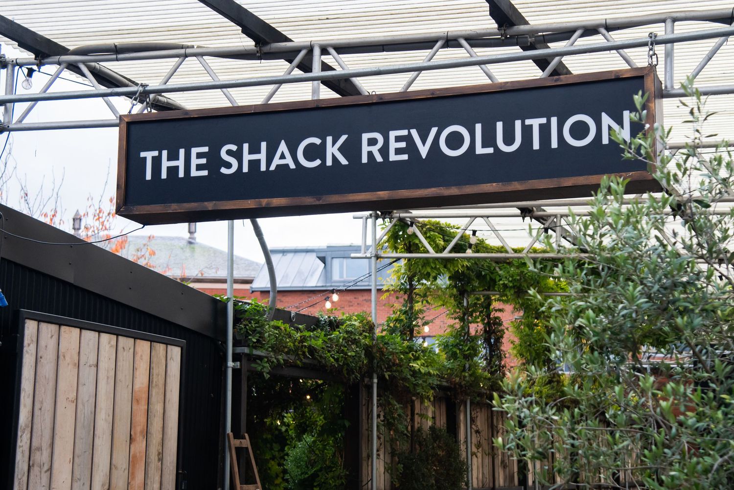 Outdoor signage reading 'The Shack Revolution' with wooden panels and metal framework.