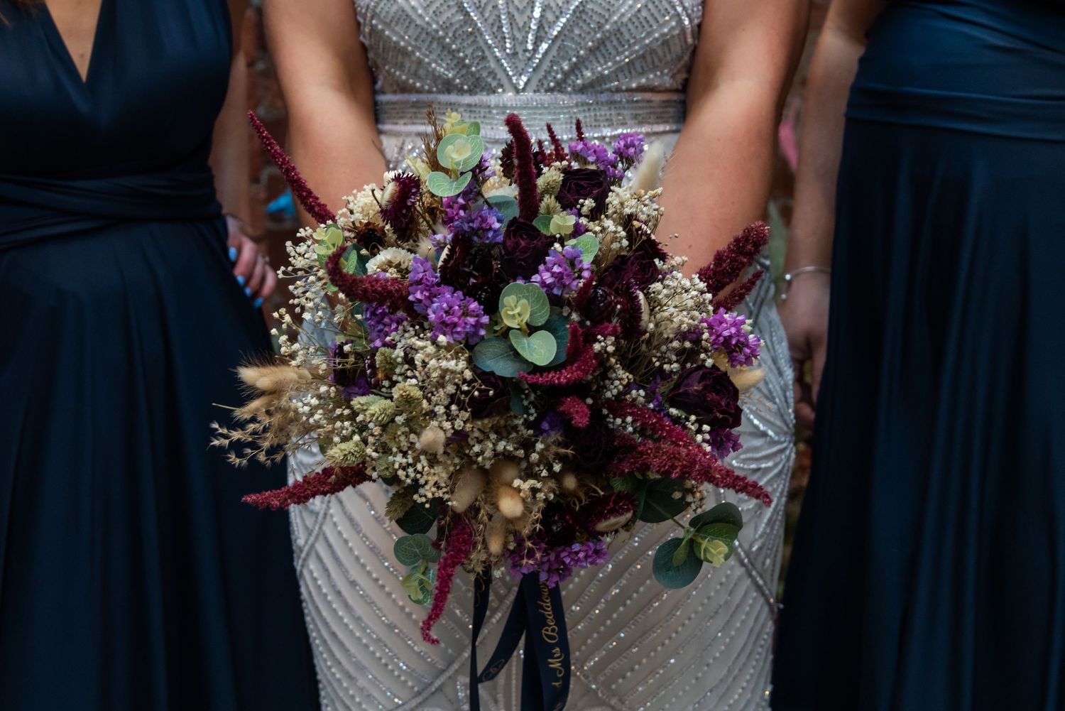 A detailed wedding bouquet with pink and purple flowers against a navy blue dress.
