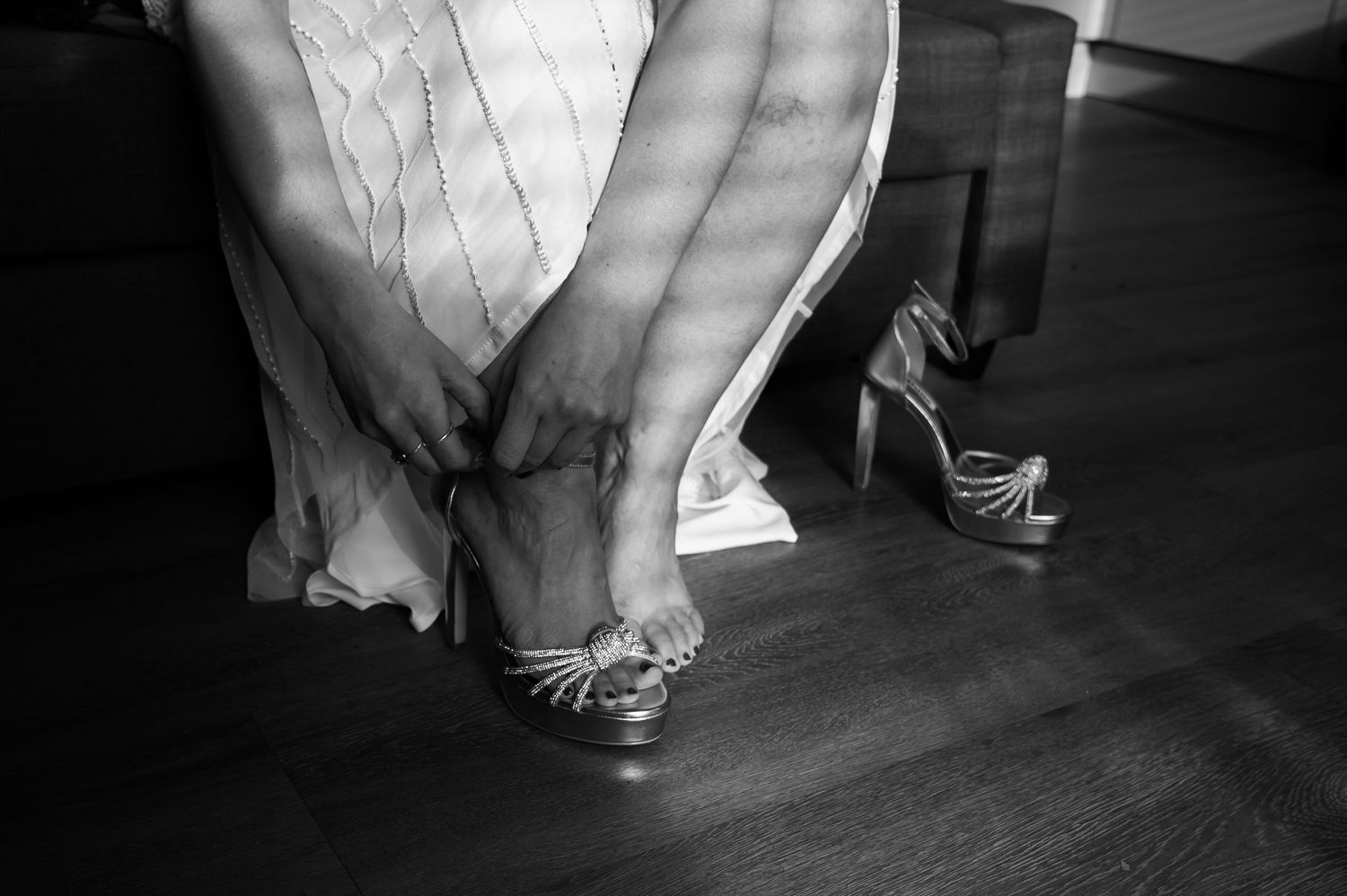 Close-up details of elegant bridal shoes and dress hem on a dark floor.