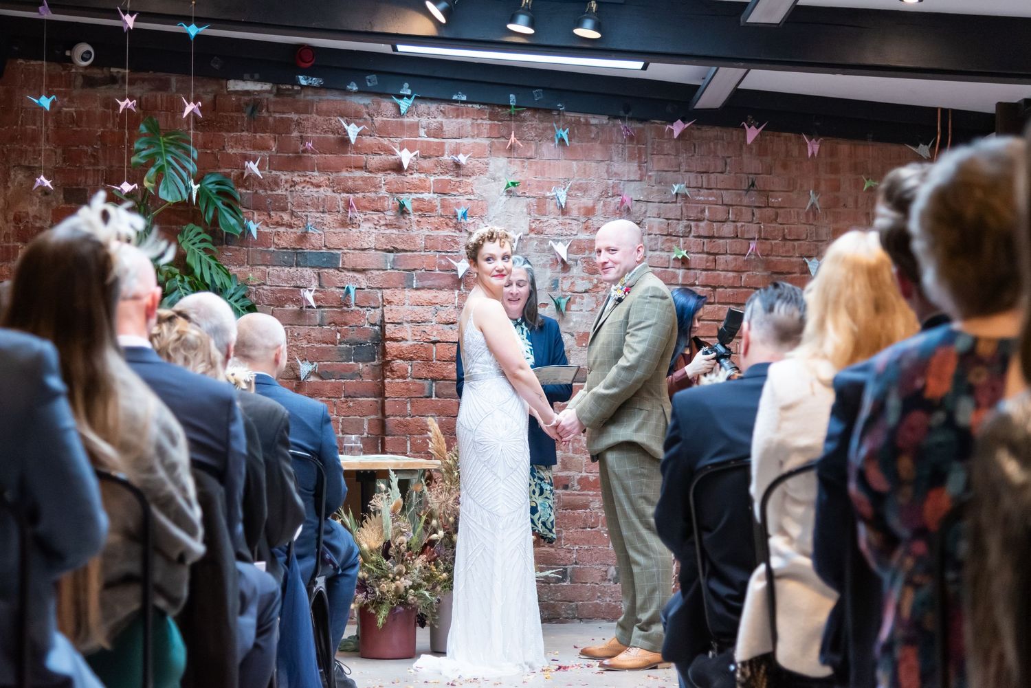 Wedding ceremony guests gathered in industrial-style venue with exposed brick walls.