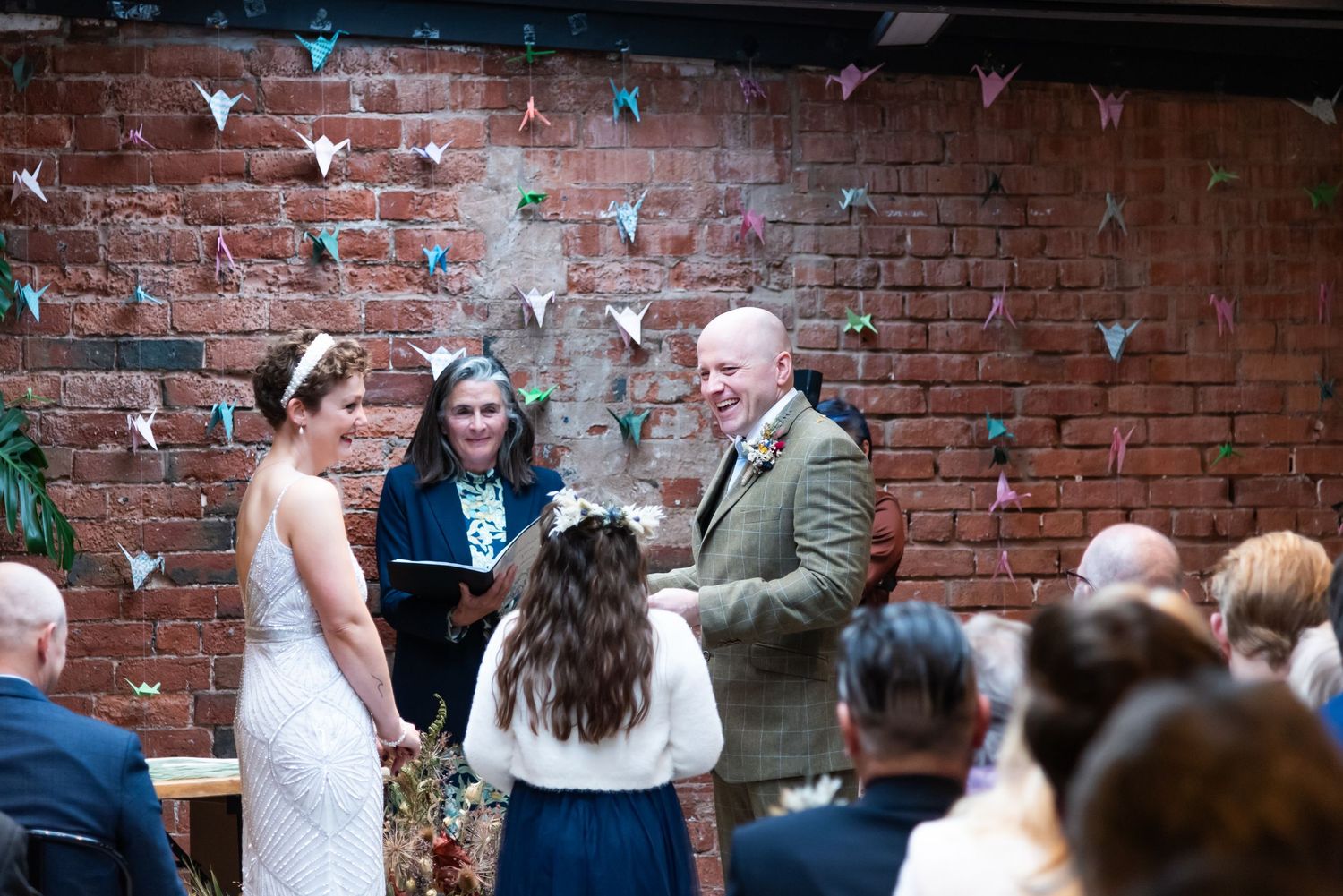 A joyful wedding celebration moment in front of an exposed brick wall with festive decorations.