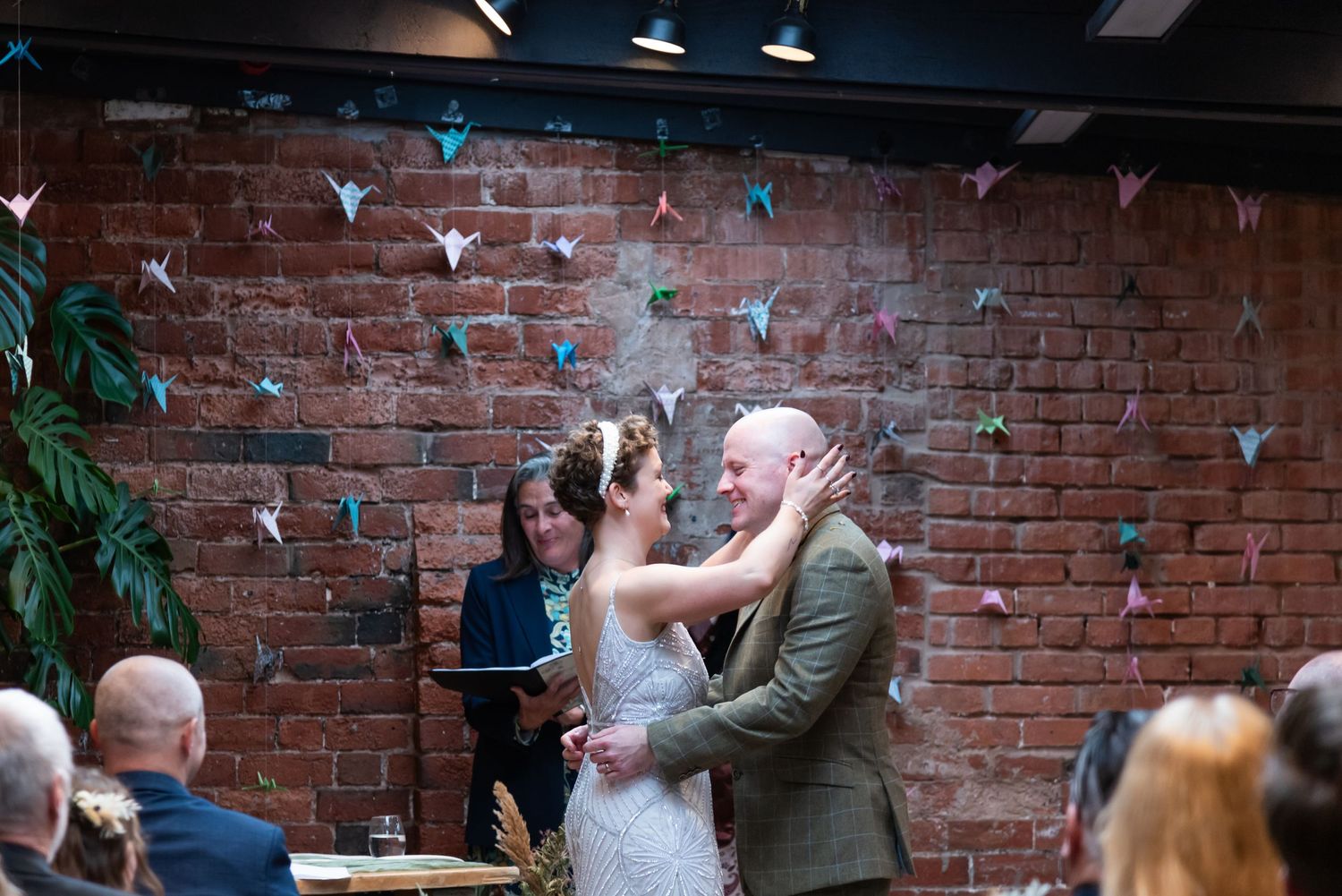 Wedding guests gathered in an intimate indoor venue with brick walls and decorative lighting.