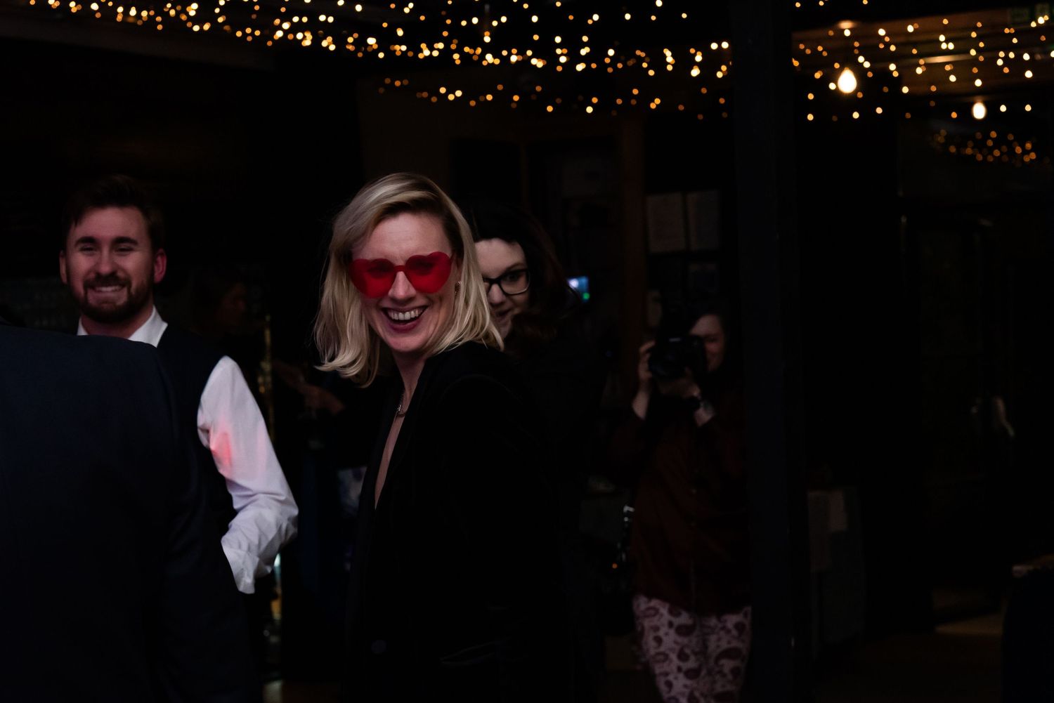 Party guests celebrating in a venue decorated with warm string lights.