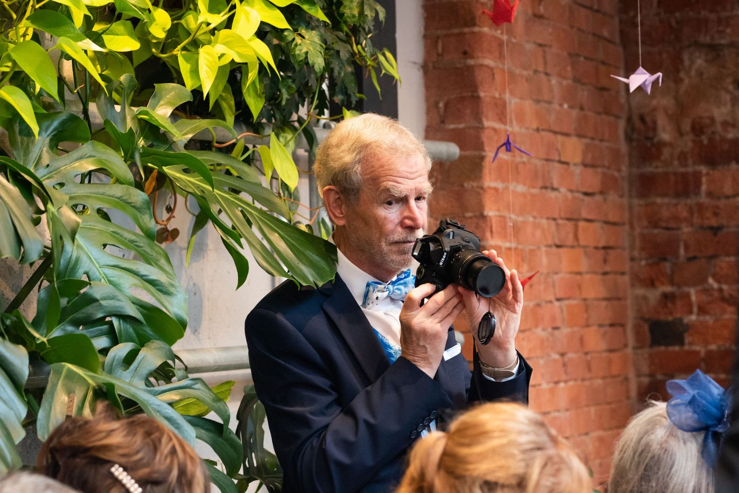 Wedding guests enjoying conversation near brick wall with lush greenery.