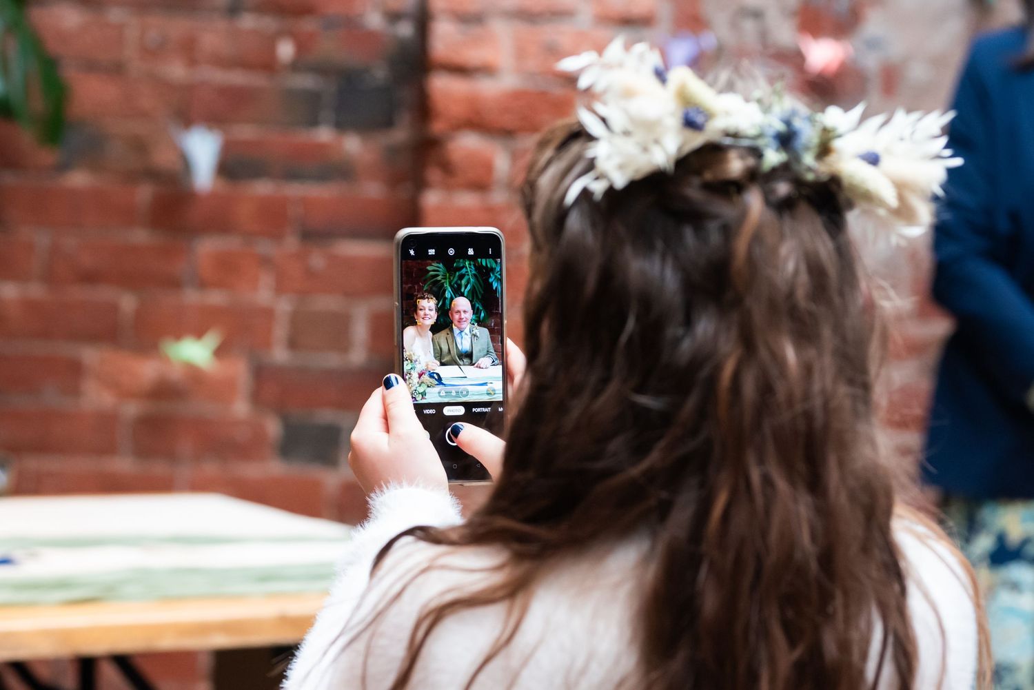 Wedding guests taking photos of cake cutting moment against brick wall backdrop.