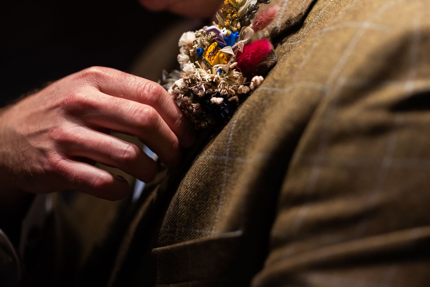 Close-up of boutonniere with gold and red details on formal attire.