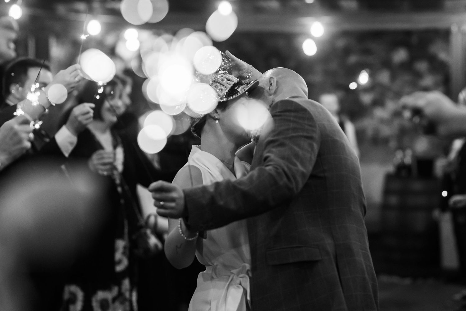 Black and white photo of couples dancing at a reception with bokeh lighting effects.