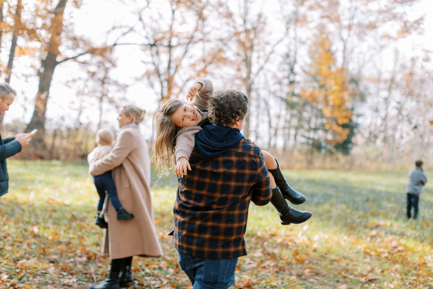 Family walking through autumn trees with fallen leaves on the ground.