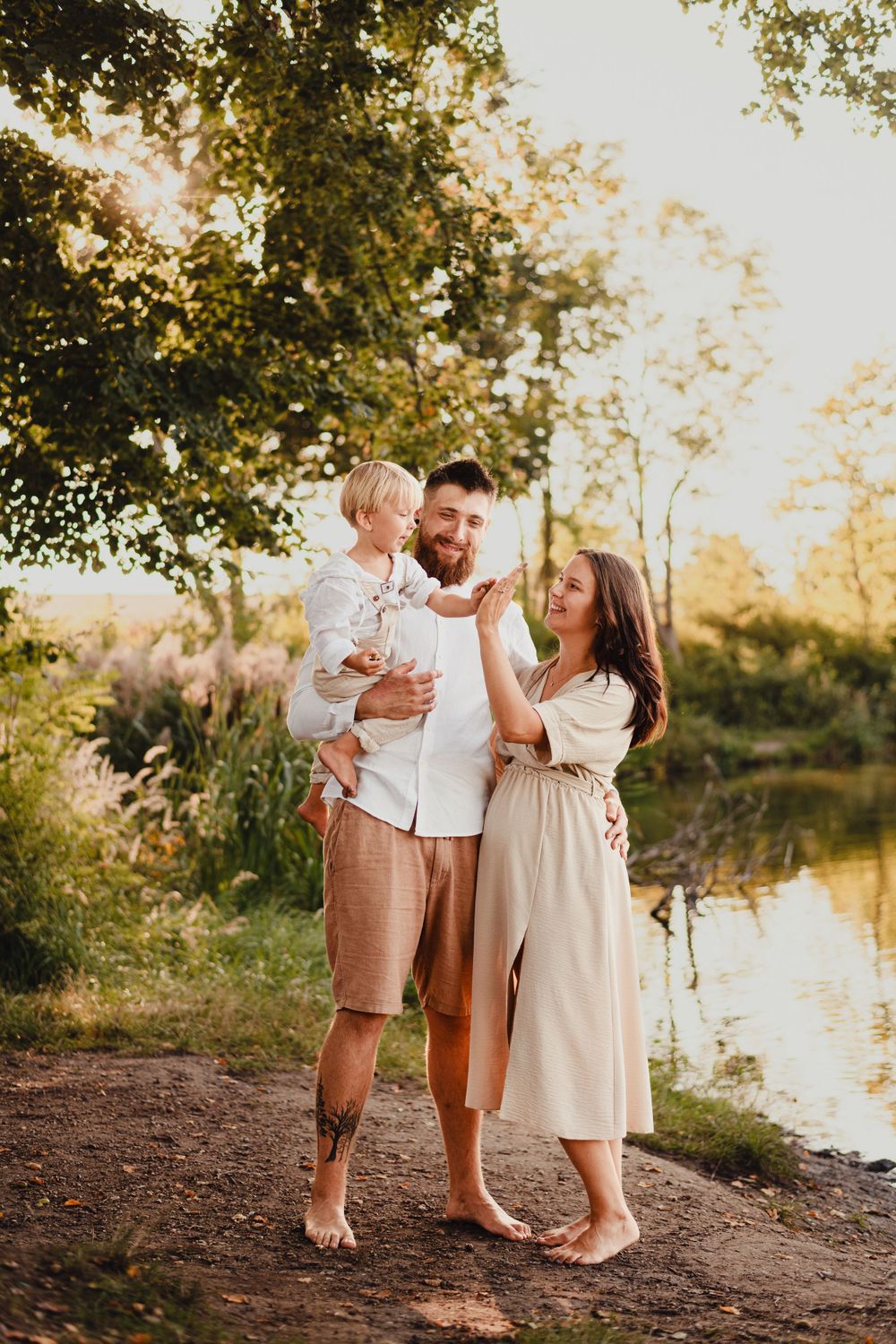 Family in matching white and beige outfits laughs together during riverside sunset session.