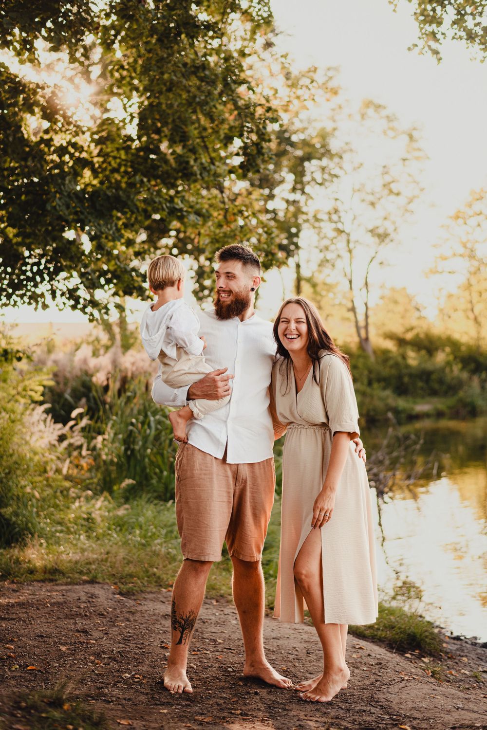 Family in coordinating neutral outfits poses together by a serene lake during golden hour sunset.