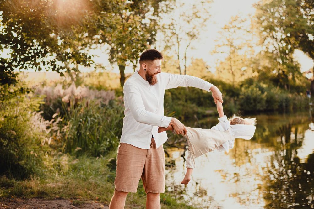 Candid family moment captured at sunset by a tranquil lake with trees in background.