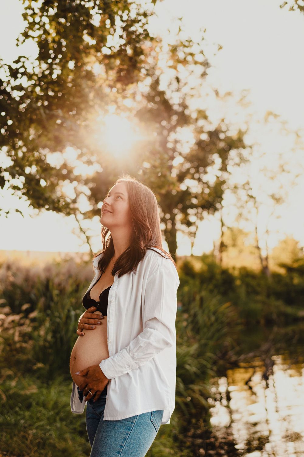 Maternity photo session in natural setting with sunlight streaming through trees.