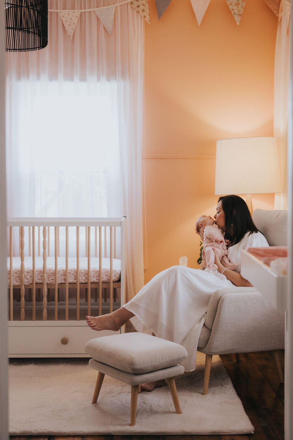 Nursery room interior with white crib, peach walls, and decorative bunting flags.
