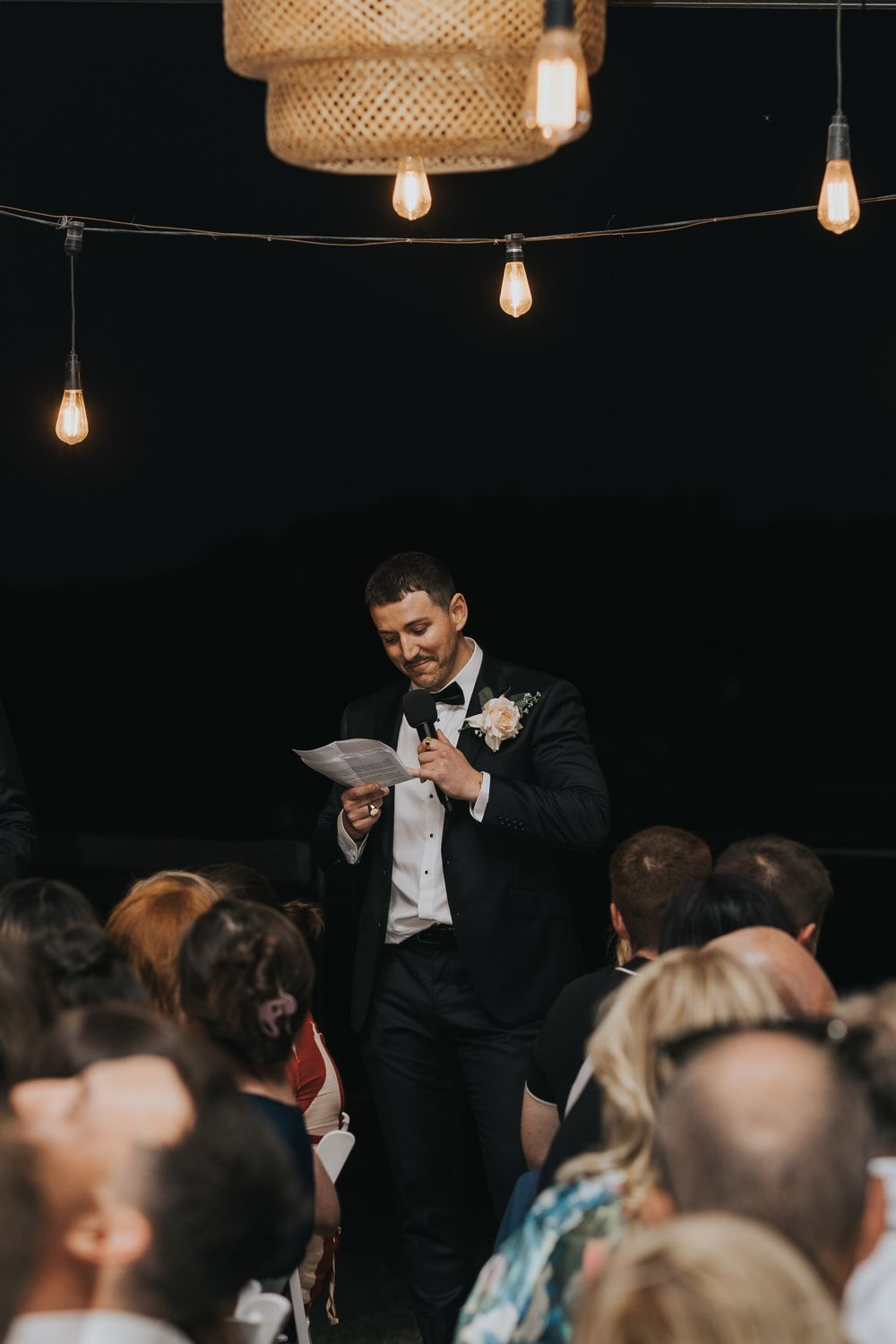 A candid moment of laughter and joy during a wedding reception with string lights overhead and guests in attendance.