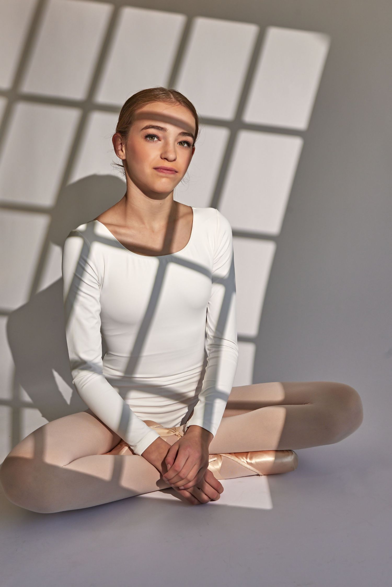 Minimalist portraits with window shadow patterns creating geometric shapes on white outfit.