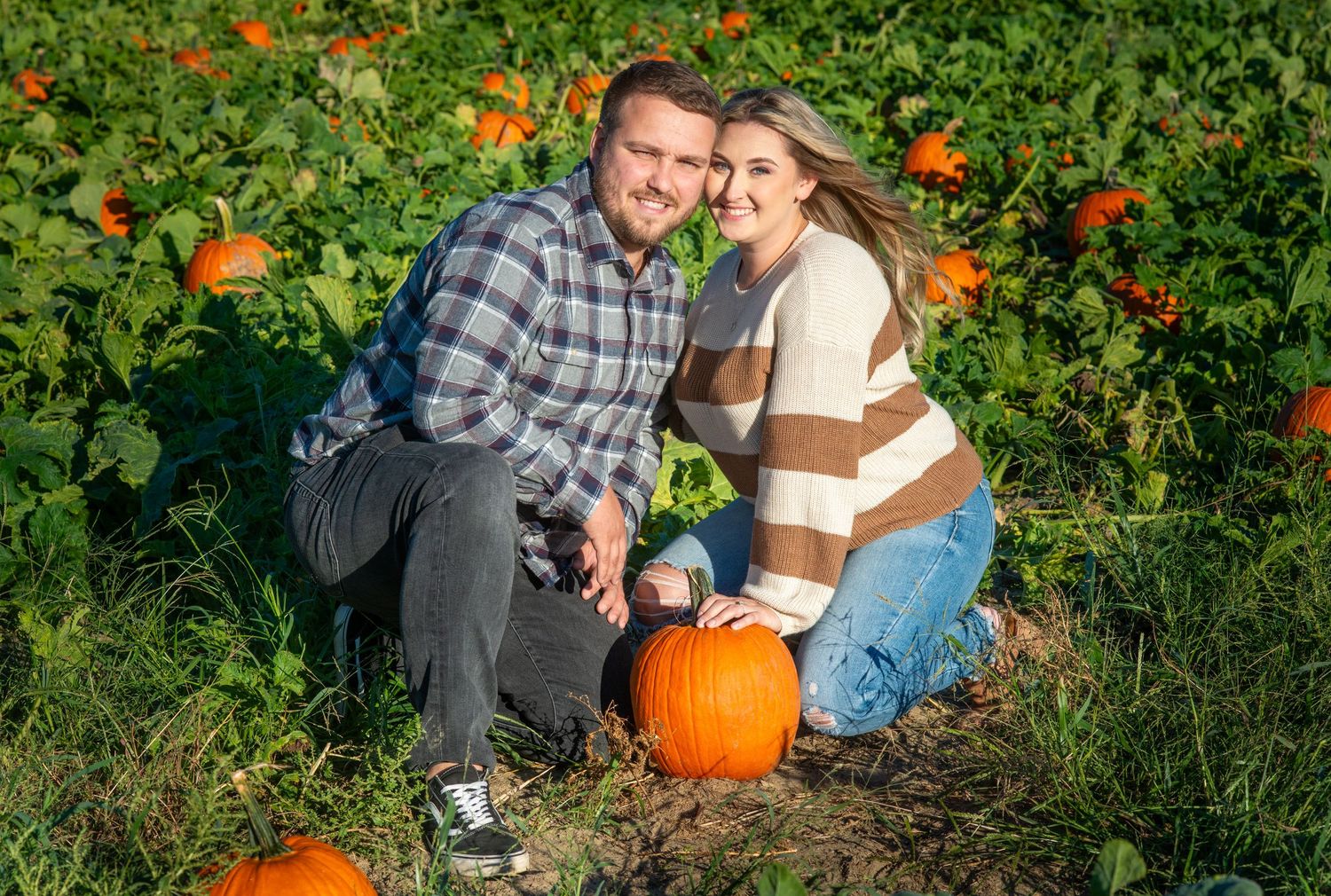 A couple poses in a pumpkin patch during an autumn engagement photoshoot.
