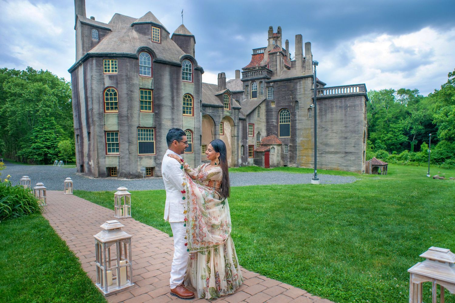Wedding couple poses in front of historic castle architecture on manicured grounds.