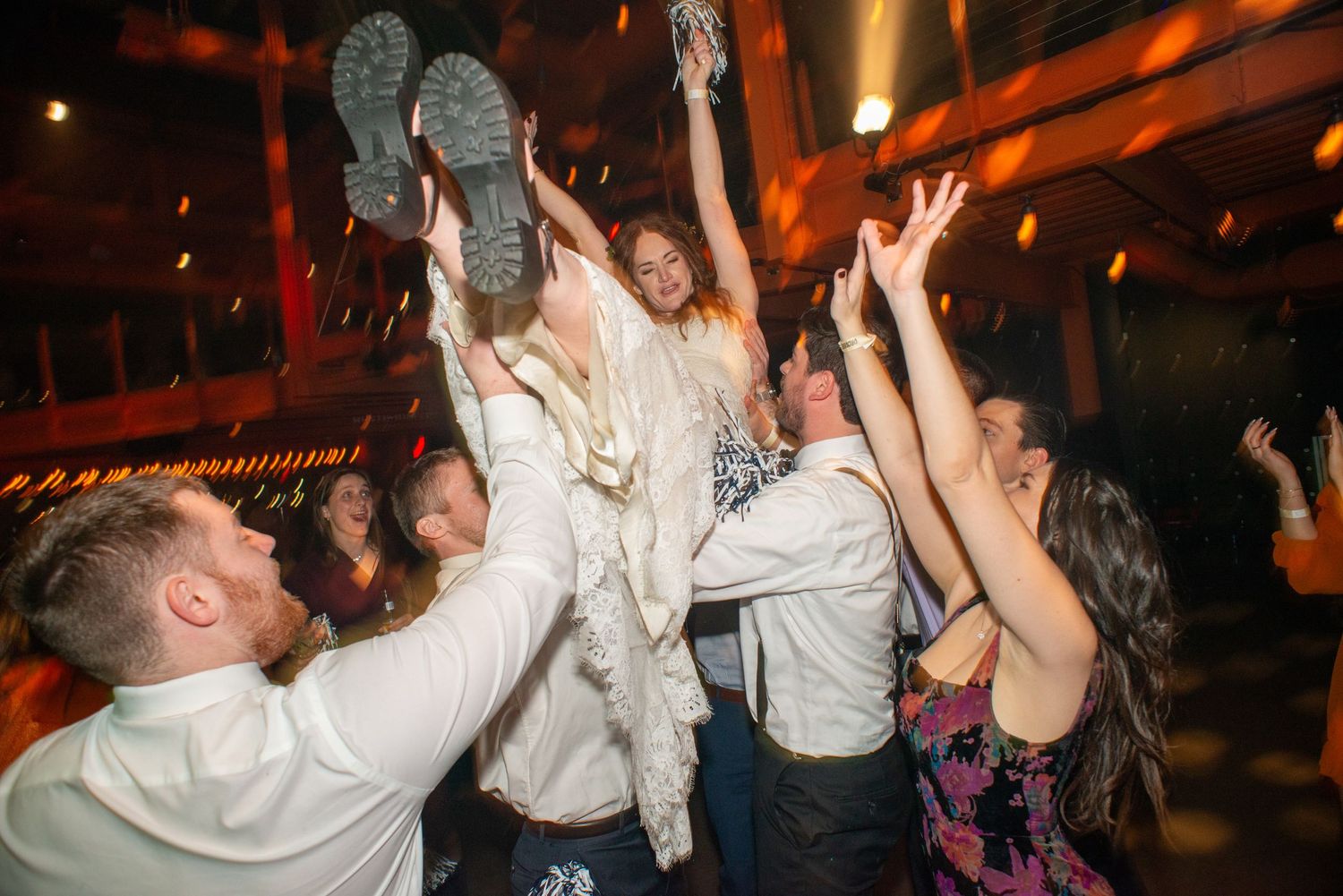 Wedding guests lift and celebrate with couple during lively dance floor reception moment.