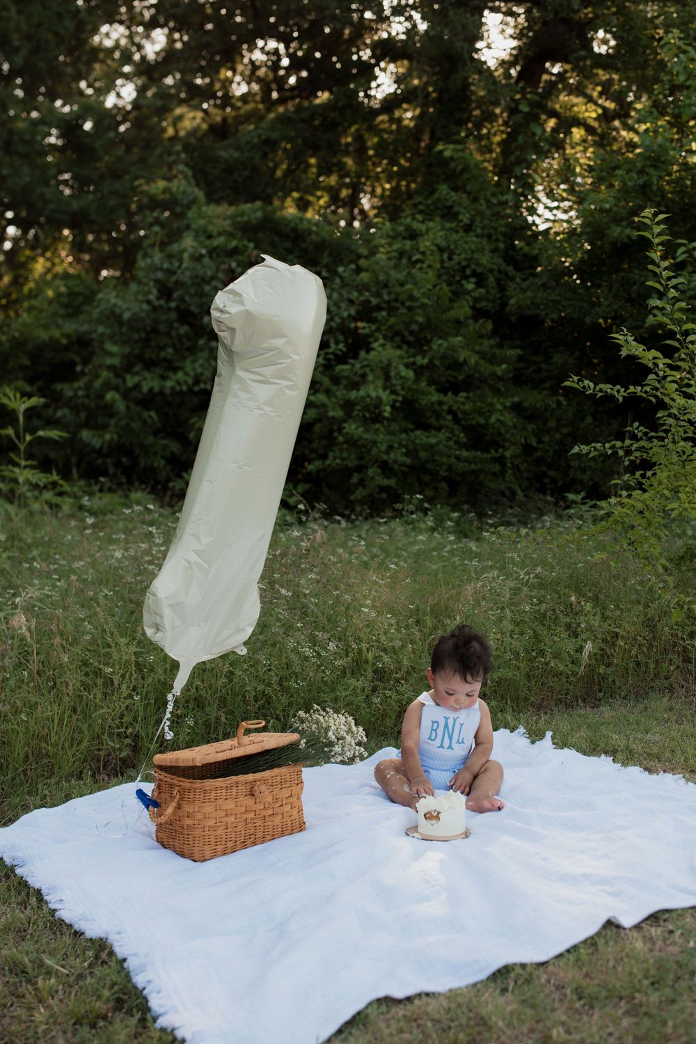 A white dress display setup in a garden setting with picnic blanket and wicker basket arrangements.