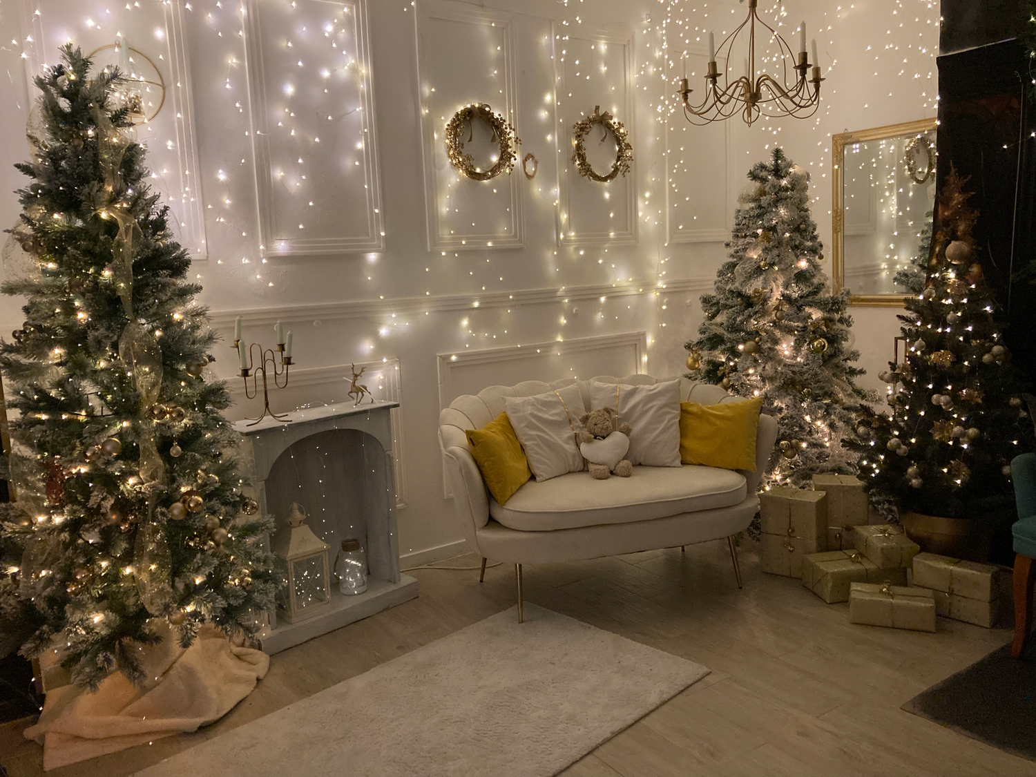 Cozy Christmas room with lit trees, fairy lights, and white settee decorated in gold accents.