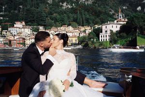 Bride and groom kissing on a boat with scenic Lake Como village backdrop on their wedding day.
