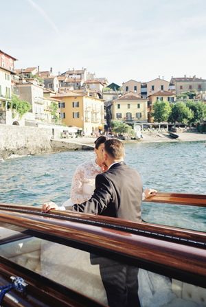 Bride and groom share romantic moment on boat overlooking Italian lakeside village.