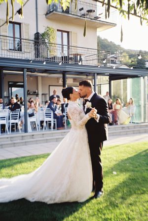 Bride and groom share their first dance on a lawn with guests seated at outdoor wedding reception.