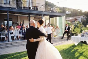 Bride and father share first dance at outdoor wedding reception with guests watching near elegant venue.