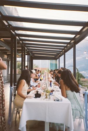 Guests seated at a long elegant table under a glass pergola at an outdoor wedding reception with mountain views.
