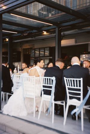 Bride and groom seated with guests at elegant evening wedding reception under modern covered terrace.