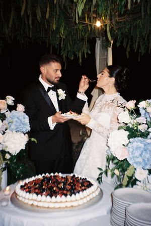 Bride and groom cutting wedding cake at elegant reception with blue hydrangeas and white floral arrangements.