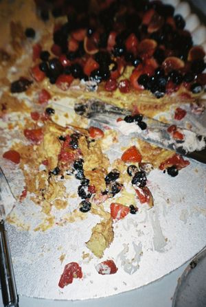 Partially sliced berry cake with whipped cream, fresh blueberries, and red fruit topping on a white plate.