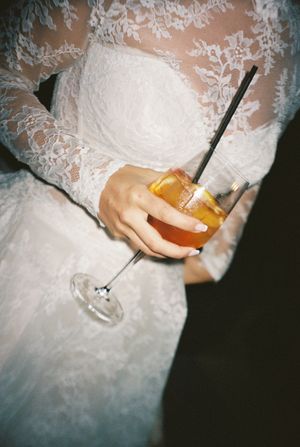 Bride in lace wedding dress holding a cocktail with a straw at a wedding reception.
