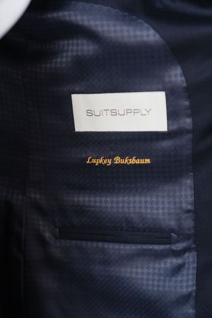 SuitSupply navy blue suit jacket interior lining with personalized gold embroidered name tag detail.