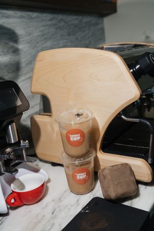 Two Lucky Cup iced coffee drinks on a marble counter beside an espresso machine and a chocolate treat.