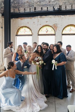 Wedding party celebrating with bride and groom in elegant venue with stained glass windows, bridesmaids in blue gowns.