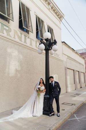 Bride and groom posing by a street lamp outside a building on their wedding day.