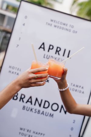 Two hands toasting with orange cocktails at April and Brandon Buksbaum's wedding at Hotel Haya, Tampa Florida.
