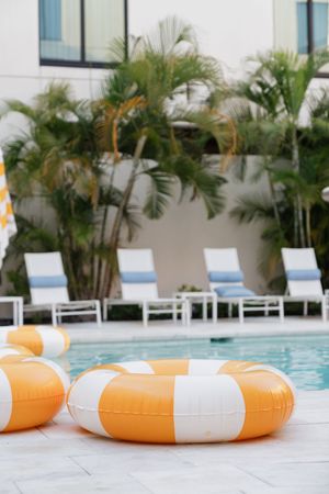 Orange and white inflatable pool rings beside a resort swimming pool with lounge chairs and palm trees.