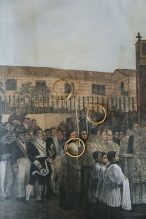 Historical painting of a religious procession with clergy and crowds, overlaid with gold rings, in a colonial town square.