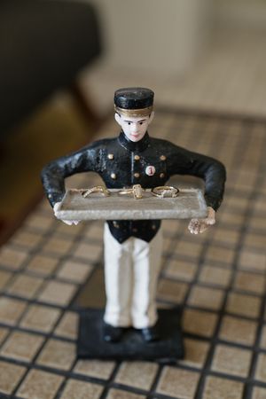 Vintage bellhop figurine in black uniform holding a gray tray, displayed on a tiled surface.