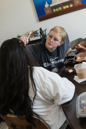 Two people sitting at a table, one with short blonde hair and glasses wearing a The Swamp shirt, engaged in conversation.