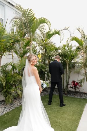 First look wedding photo with couple in outdoor garden setting surrounded by lush tropical palm trees.
