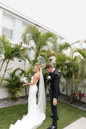 A bride and groom share a romantic moment in a garden courtyard surrounded by tall palm trees and white walls.